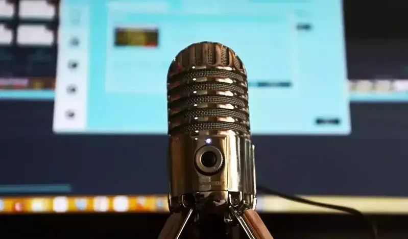 Microphone in focus with blurred screen showing audio-streaming software, representing CastHost internet-radio broadcasting and hosting services