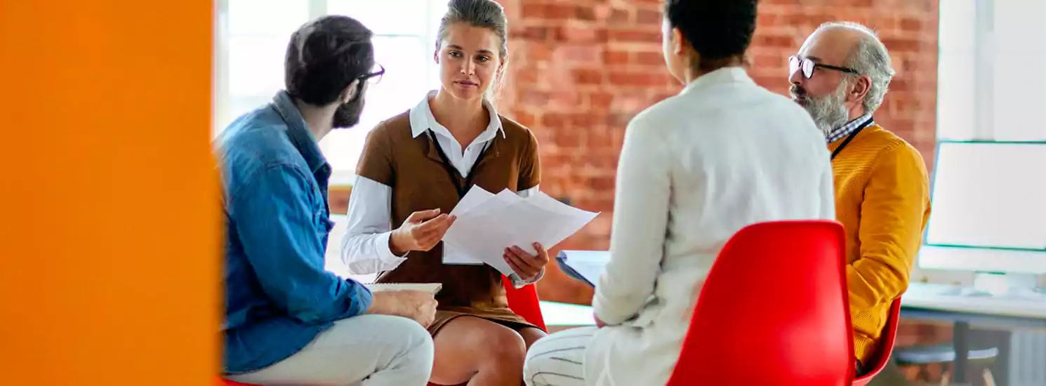 Discussion de groupe entre quatre personnes dans un bureau moderne, axée sur la collaboration et le brainstorming pour les services d'hébergement radio en ligne.